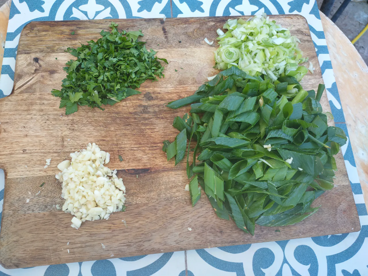 Chopped parsley, sliced spring onions, shredded wild garlic, and minced garlic arranged on a wooden chopping board