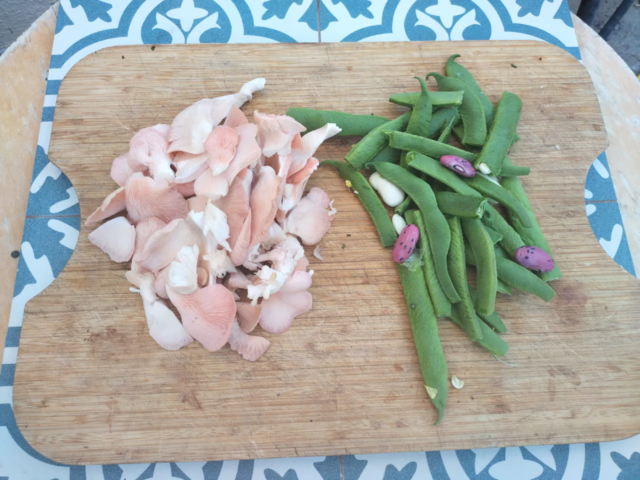 Torn pink oyster mushrooms and green beans arranged on a wooden chopping board, ready for the wok